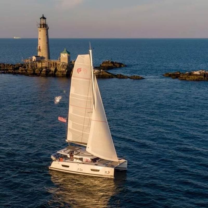 Catamaran off the coast of Boston with a lighthouse in the background