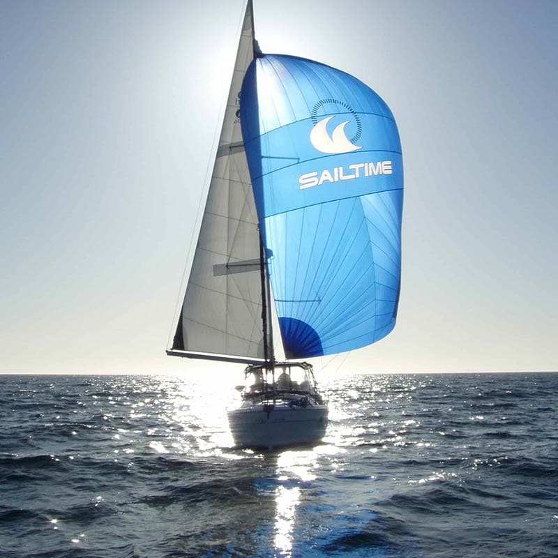 Sun shining behind a gennaker sailboat with SailTime logo on sail