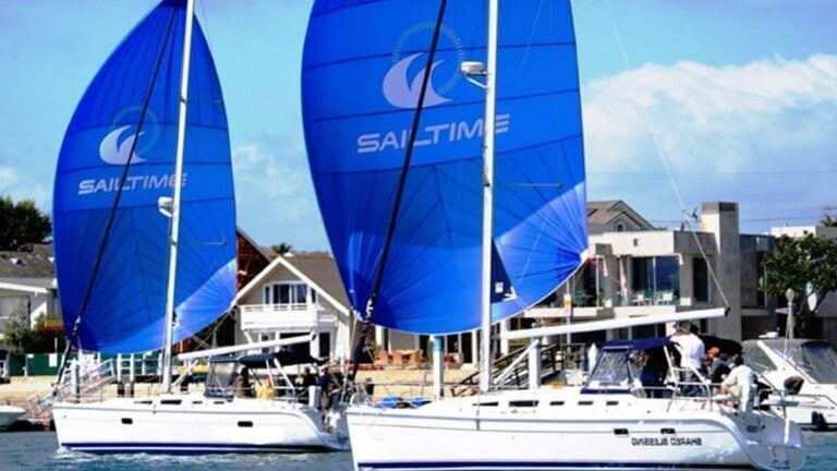 Sailboats moving out of port with SailTime logos on sails