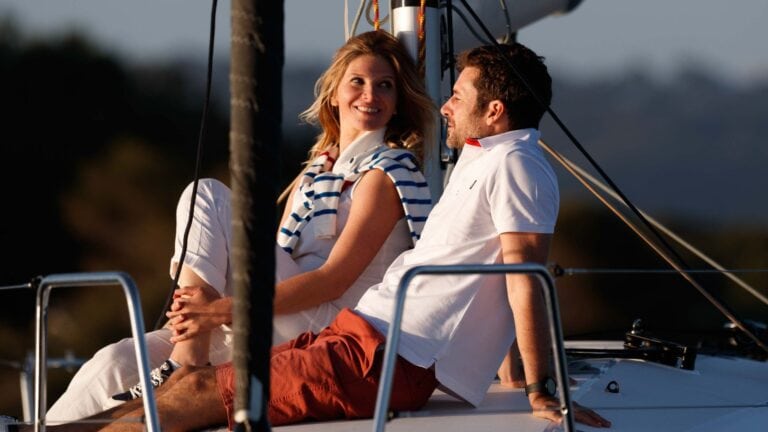 A man and a woman sitting on the Jeanneau Sun Odyssey 350 at sunset.