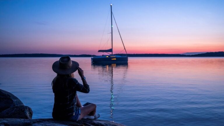 A woman sitting on the shore with a Beneteau Oceanis 30.1.